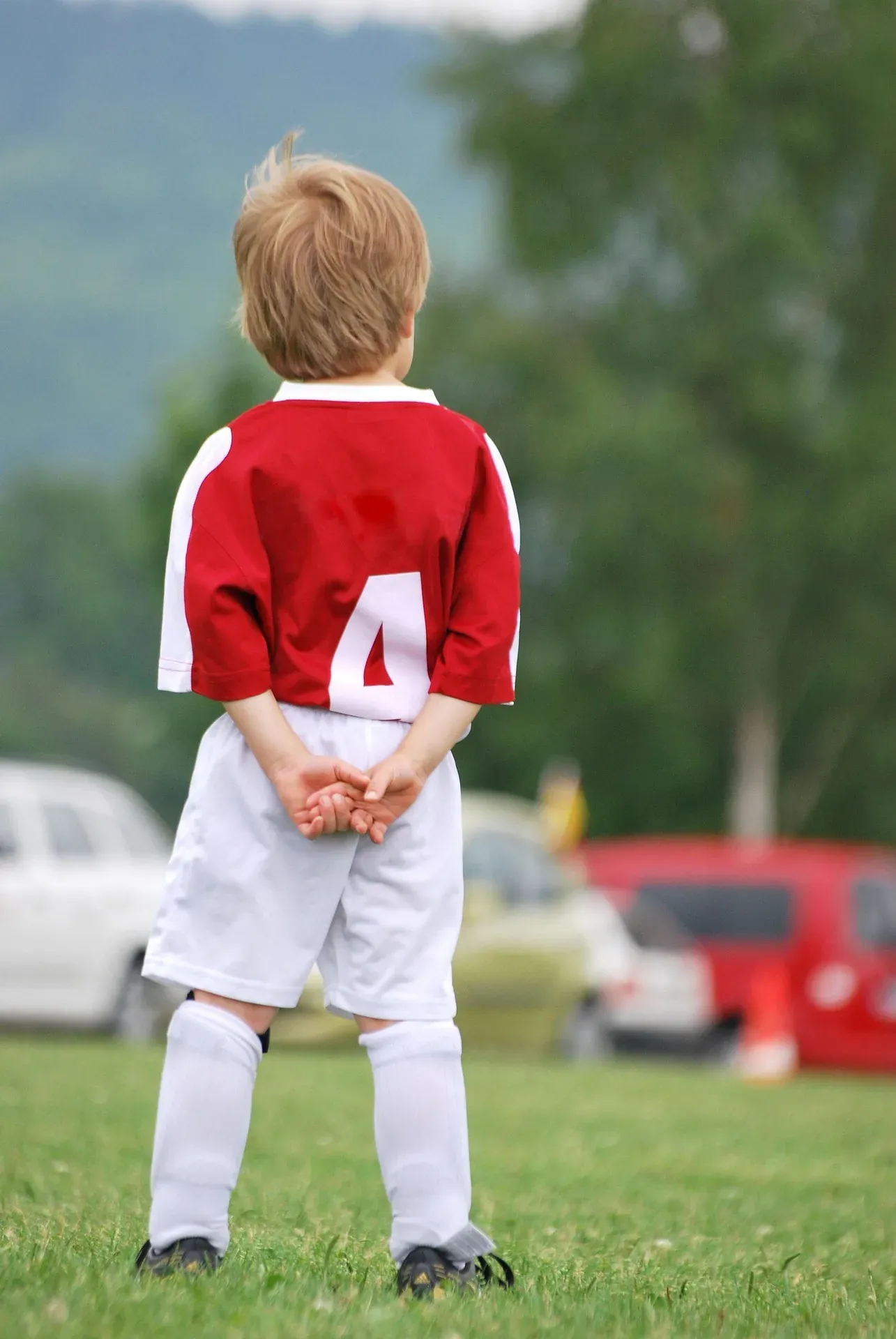 A young footballer in a red and white kit waiting on the sideline.