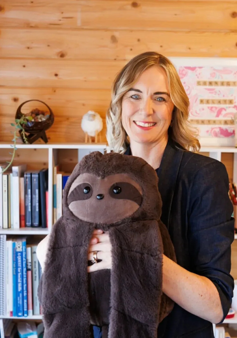Emily Baird holding a large soft sloth toy in her practice room.