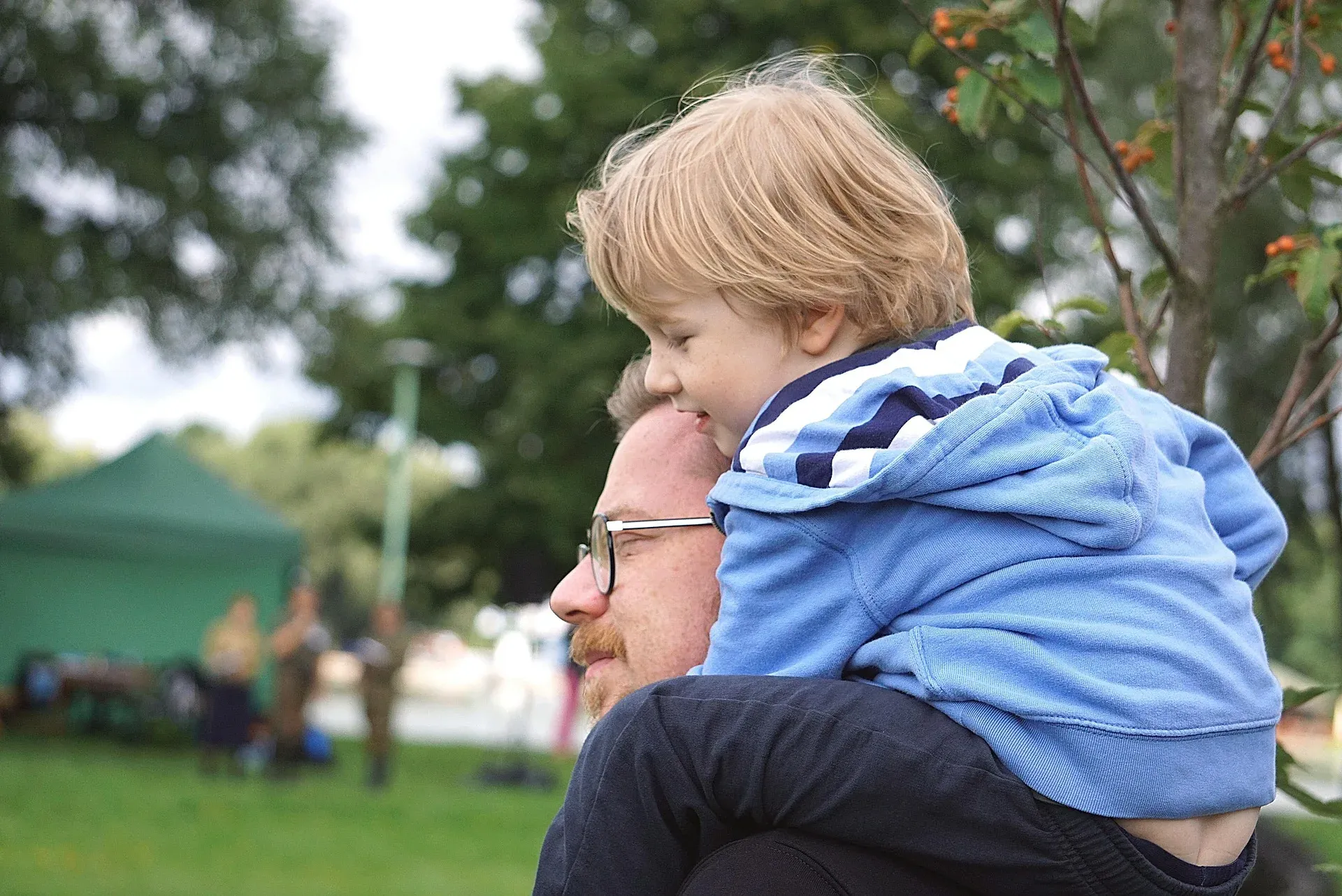 A father carrying his young son on his shoulders at a park.