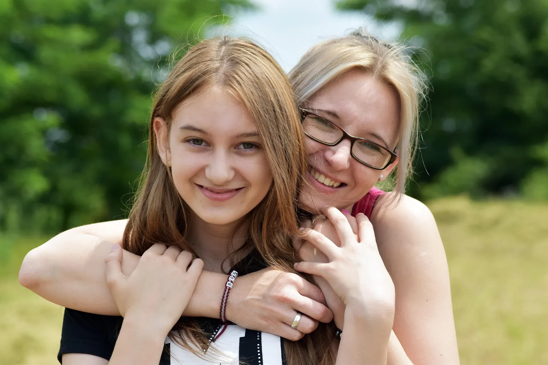 A mother and teenage daughter smiling together outdoors.